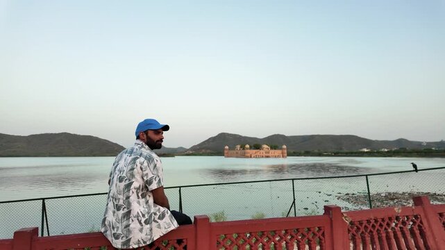 A man with a blue cap looks out at Jal Mahal from a railing.