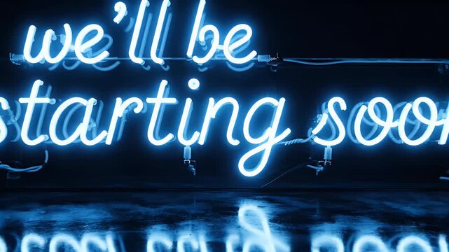 A vibrant blue neon sign displaying the message 'we'll be starting soon' is reflected in a dark, glossy surface, creating a captivating and futuristic aesthetic.