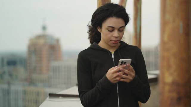 African American woman texting on phone on rooftop, upset about bad news