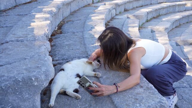 Woman using smartphone while petting a cat at Teos ancient theater ruins