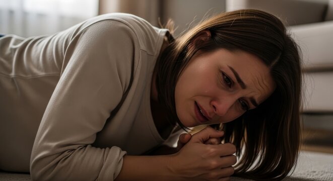 woman collapsing in grief, a person sitting on the floor in distress with her face buried in her hands. This image represents mental health issues, depression, loss, mourning, and emotional psychologi