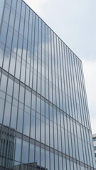 Naklejka premium Modern Glass Office Building Facade Reflecting Soft White Clouds Low Angle