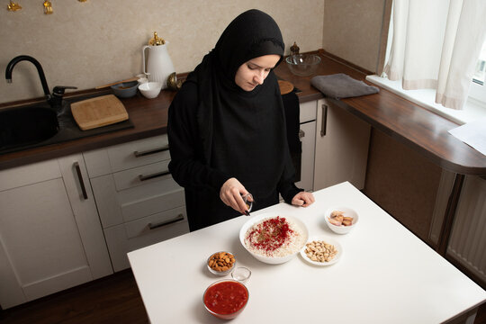 overhead view of a woman in black modest clothing seasoning a bowl of rice in a home kitchen, combining food preparation, cultural cooking and festive meal concepts