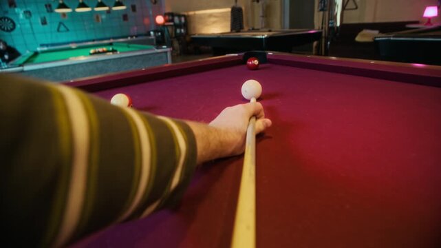 POV shot of unrecognizable man aiming shot on red felt pool table then potting ball with precision while playing billiards in game room