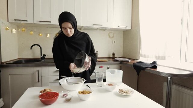 woman in black hijab pours dry long grain rice from a glass bowl into a sieve set over a white bowl, showing a practical prep step before washing and cooking