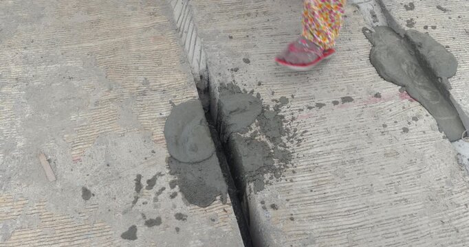 Close up of wet concrete being poured into an expansion joint on a bridge road surface, next to a worker's foot in a floral sock and sandal.