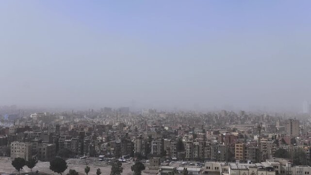Panoramic view above dusty Cairo skyline, Egypt, with towering minarets and massive stone domes in medieval Islamic architecture.