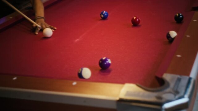 Tilt down shot of young adult African American man lining up shot then pocketing ball in billiards on red felt table while spending weekend night out with female friend at pool hall