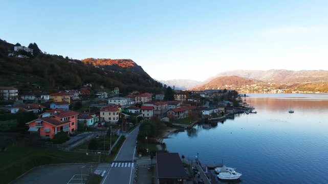 Pella, picturesque village with colorful houses on shore of Lake Orta during golden hour in Piedmont, Italy. Aerial forward, copy space