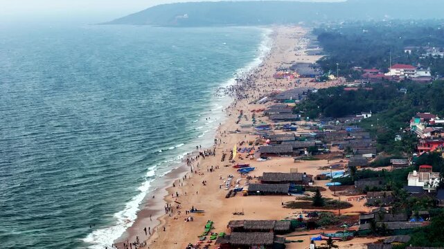 Drone shot capturing the bustling stretch of Baga Beach, filled with crowds, beach activities, and rows of huts, blending movement, color, and ocean waves.