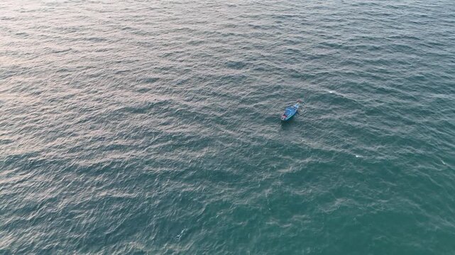 Cinematic aerial view of a lone boat drifting across textured ocean waters, surrounded by gentle ripples and soft reflections. The vast open sea emphasizes isolation and calmness.