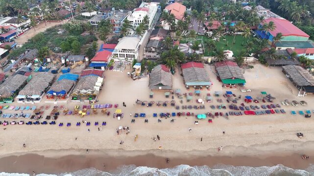 Cinematic lateral drone shot moving left along a vibrant beach, revealing rows of colorful sunbeds, beach shacks, and palm-lined resorts as waves gently wash the shoreline.