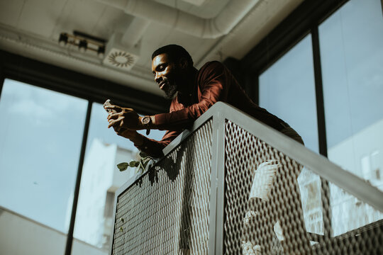 Man using phone while standing on balcony during bright day inside building