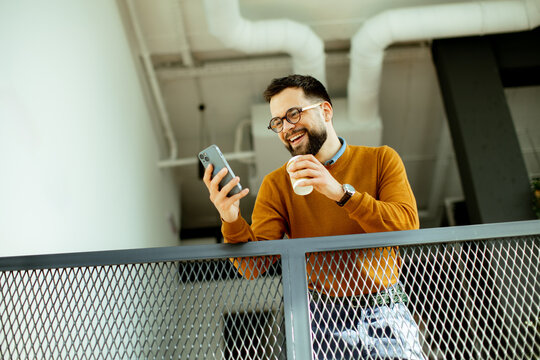 Joyful man enjoying coffee and smartphone at a modern indoor space