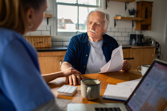 Caregiver helps senior man review paperwork at home kitchen table