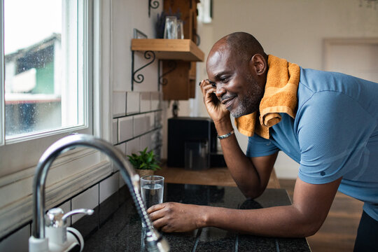 Smiling man talking on phone by kitchen sink