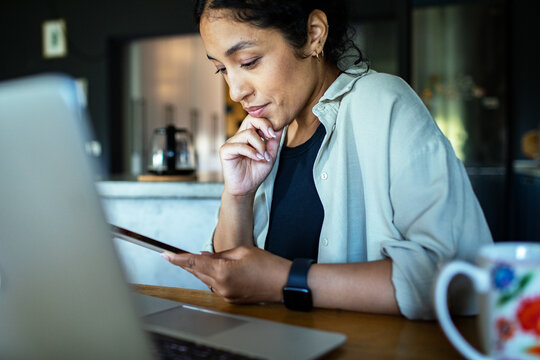 Woman working from home with smartphone and laptop in kitchen