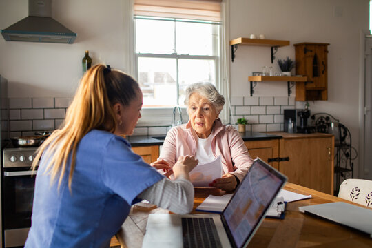 Nurse consulting with senior woman over paperwork at home kitchen