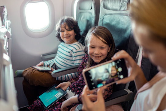 Two children with tablets on airplane as parent takes photo