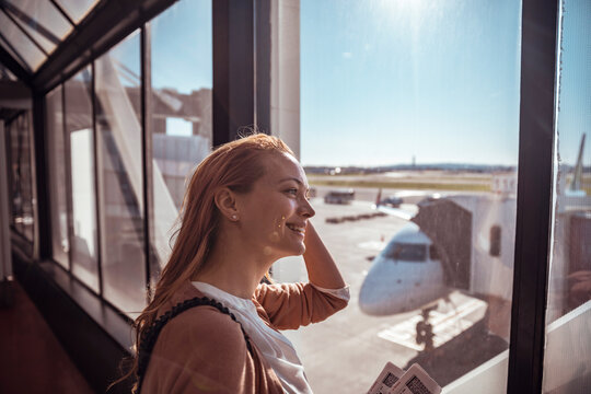 Smiling traveler holding ticket at airport gate window