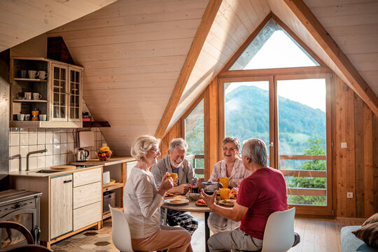 Senior friends laughing over breakfast in mountain cabin kitchen