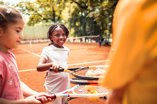 Smiling children learning tennis on outdoor clay court