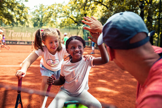 Kids high-fiving tennis coach on outdoor clay court