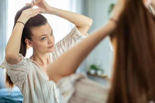 Young woman brushing hair in mirror at home