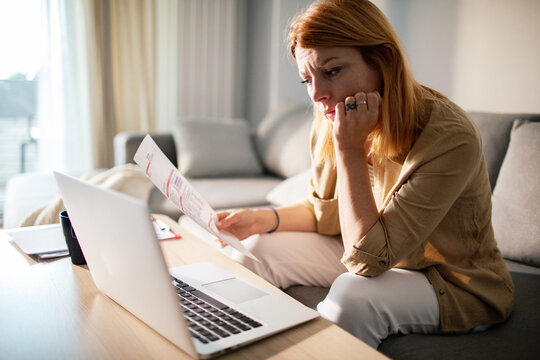 Worried woman reviewing bills at home with laptop