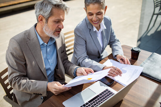 Two senior business colleagues reviewing reports at outdoor cafe