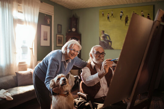 Senior couple painting together at home studio with dog