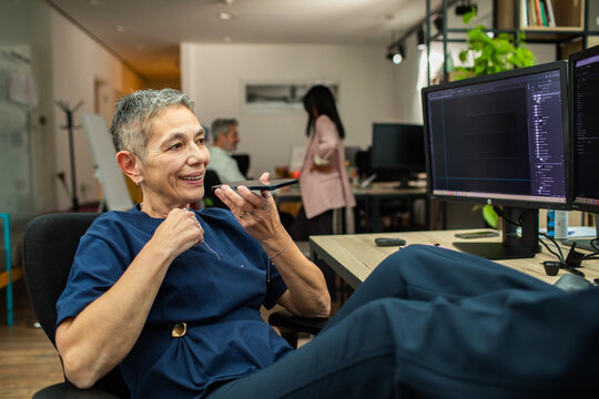 Mature professional speaking into smartphone at modern office desk