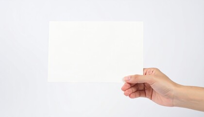 Obraz premium Hand holding blank white paper against white background for copy space