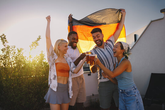 Group of diverse friends cheering and toasting beer outdoors with a german flag