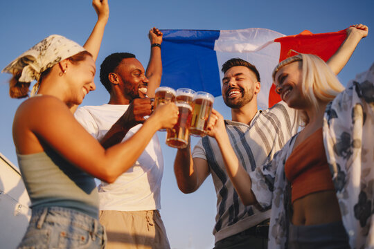 Diverse friends cheering and celebrating with french flag on rooftop