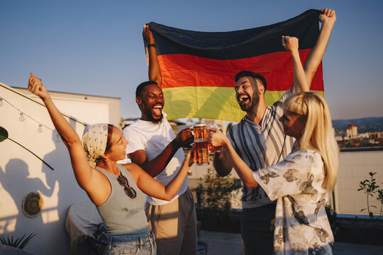 Diverse friends celebrating with germany flag and beer on rooftop