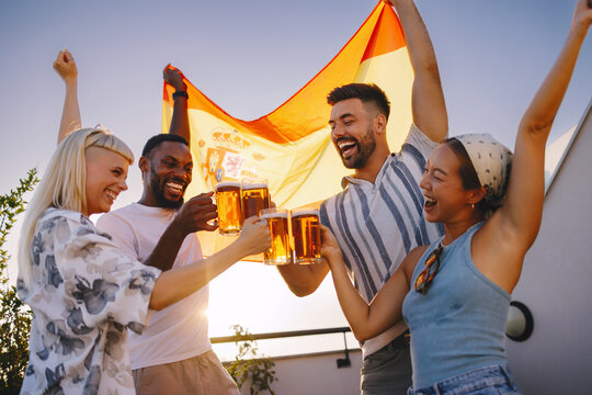 Diverse friends cheering and toasting beer with a spanish flag on a rooftop