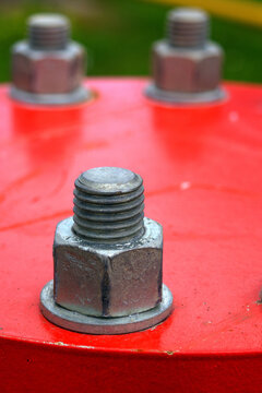 Close-up view of a metallic bolt with threads on a bright red surface. Industrial hardware detail.