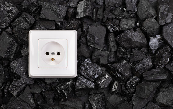 Using coal as a source of electricity concept, white plastic power outlet on a heap of black coal