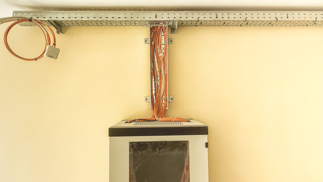 Network server rack with organized orange ethernet cables in metal cable tray on the wall