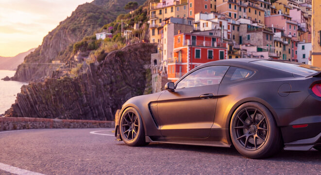 sleek matte black performance sports car driving on a scenic winding coastal road at sunset with colorful historical mediterranean village on a cliffside as concept of luxury travel and automotive exc