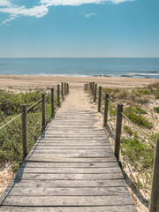 Obraz premium Scenic view of a rustic wooden walkway crossing sand dunes toward the blue sea at Sao Felix da Marinha beach in Porto Portugal under a bright sunny sky