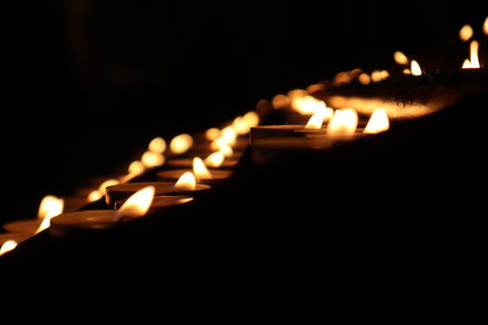 Suggestiva scia di candele accese nell'oscurit&agrave; di una chiesa, luce soffusa di fiammelle votive che creano un'atmosfera di preghiera, fede e speranza nel buio
