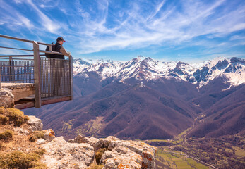A man tourist stands on a viewpoint above a valley against mountains covered with the snow. National Park Peaks of Europe (Picos de Europa). Cantabria, Spain, Europe © vvvita