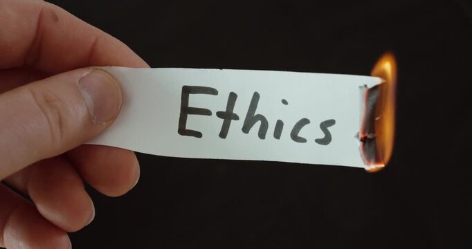 Hand burning a paper labeled &ldquo;Ethics,&rdquo; symbolizing decline of values, moral conflict, and social issues.