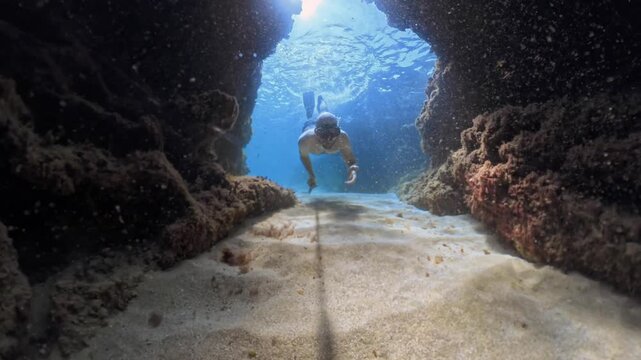 Man freediving and swimming through natural rock arch in clear turquoise water