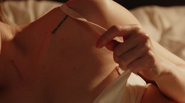 Sensual close up of an enticing woman wearing a white brassiere enticingly playing with her bra strap while lying in bed