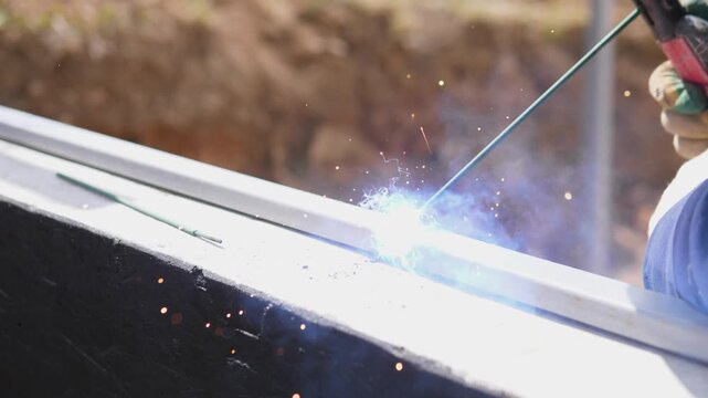 Detail Welder Finishing Rail Seam With Steady Bead, Closeup Of Glowing Arc And Tiny Sparks, Final Pass Smooths Joint For Fence Installation, Bright Daylight And Trench Backdrop On Private