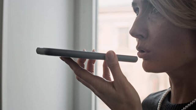 Close up of blonde employee of office recording message on smartphone while working in office of company