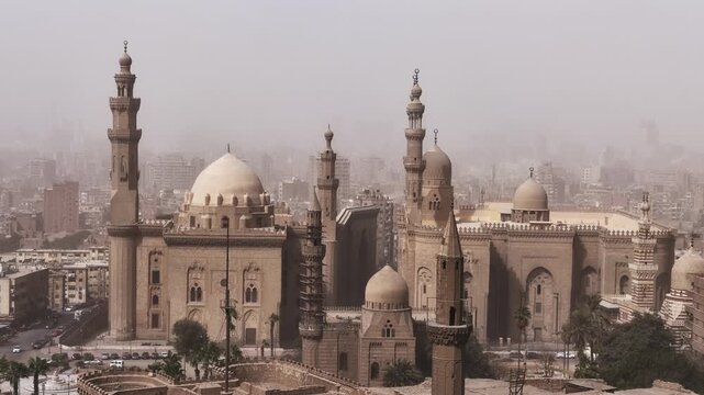 Historic mosques with tall minarets and grand domes dominate the hazy Cairo cityscape, Egypt, showcasing stunning Mamluk Islamic architecture from the medieval period.